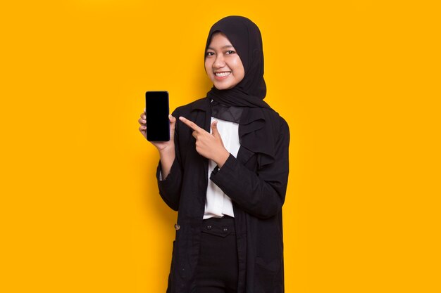 young beautiful asian muslim business woman demonstrating mobile cell phone on yellow background