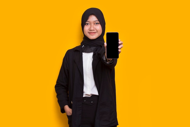 young beautiful asian muslim business woman demonstrating mobile cell phone on yellow background