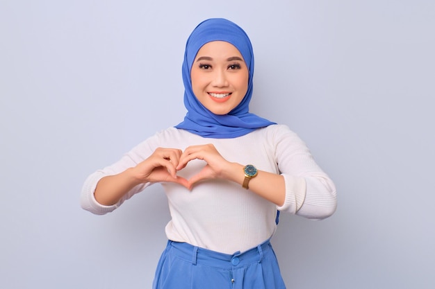 Young beautiful Asian Muslim woman showing heart gesture and smiling isolated over white background