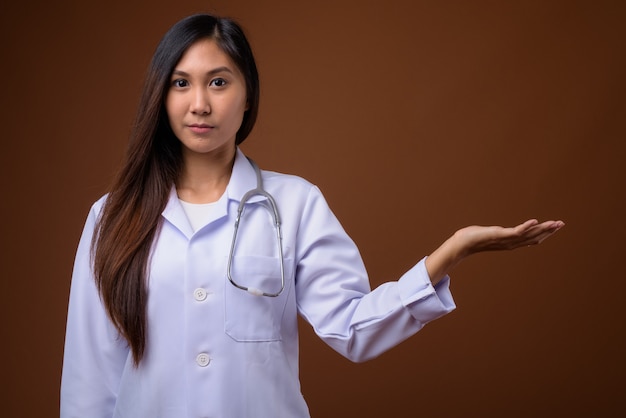 Young beautiful Asian woman doctor against brown background