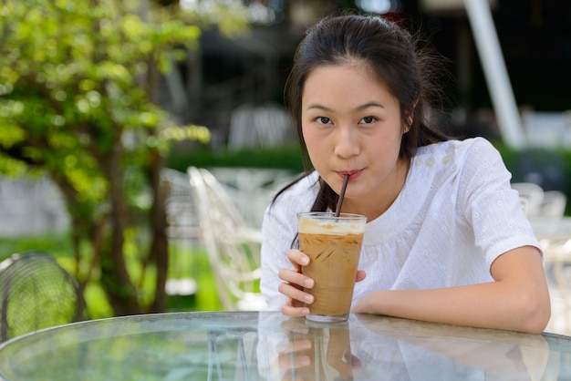 Young beautiful Asian woman drinking coffee at the coffee shop outdoors