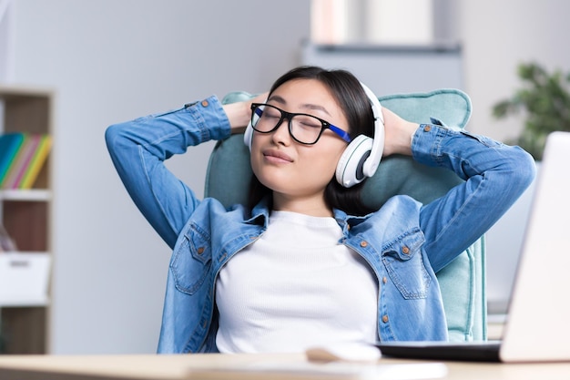 Young beautiful asian woman listening to music in headphones closing her eyes and throwing her hands