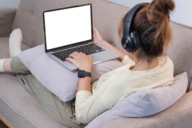 Young beautiful asian woman relaxing and listening to music using headphones she is lying in sofa Young woman enjoying at home using laptop