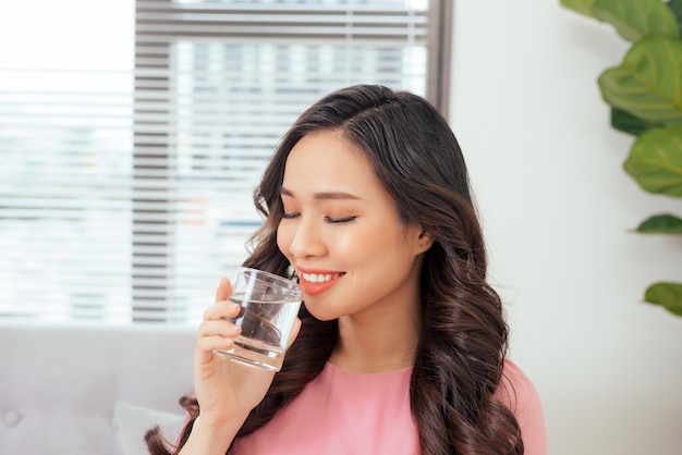 Young beautiful asian woman relaxing in sofa with cup of pure water