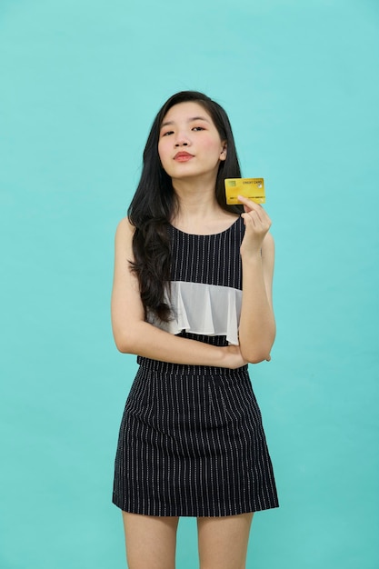 Young beautiful Asian woman smiling, showing, presenting credit card for making payment or paying online business over blue background