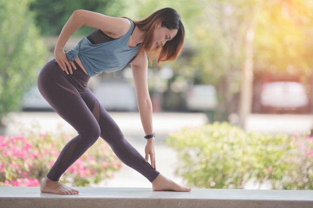 Young beautiful Asian woman in sports outfits doing stretching before workouts at hot during COVID-19 pandemic to keep a healthy life. Healthy young woman stretching and warming up to workouts