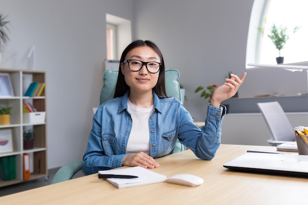 Young beautiful asian woman talking on video call business woman working in modern office smiling and looking at web camera online conference