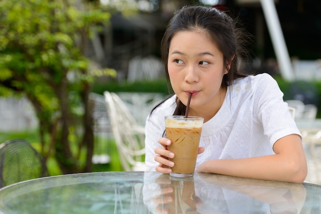 Young beautiful Asian woman thinking while drinking coffee at the coffee shop outdoors