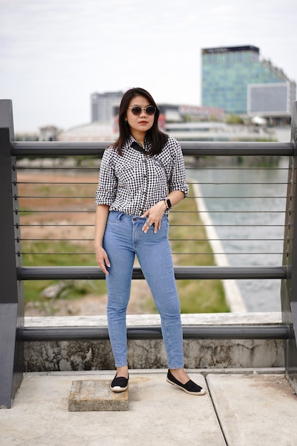 Young Beautiful Asian Woman Wearing Plaid Shirt And Blue Jeans Posing Outdoors