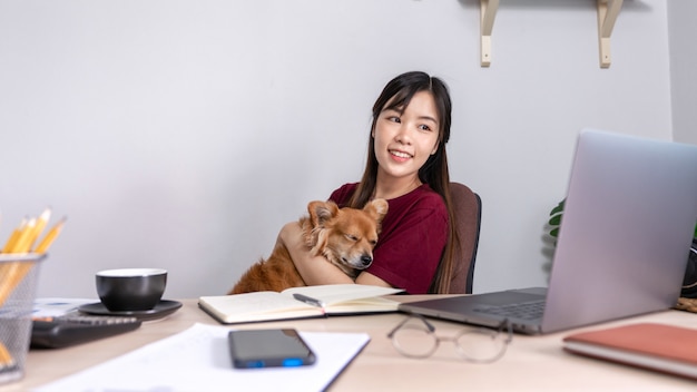 Young beautiful asian woman working at home with her dog