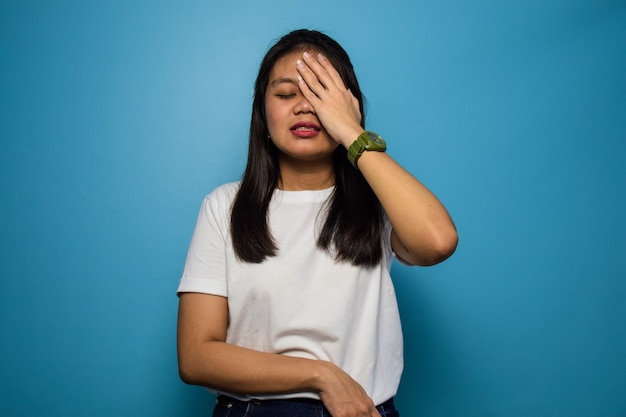 Young beautiful asian women using white Tshirt with blue isolated background headache gesture