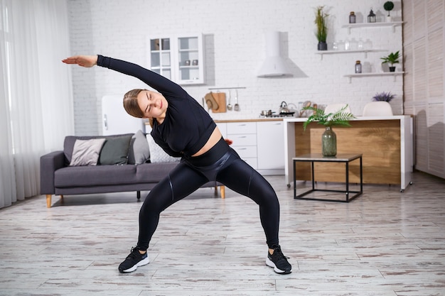 Young beautiful athletic girl in leggings and a top does stretching exercises. Healthy lifestyle. The woman goes in for sports at home.