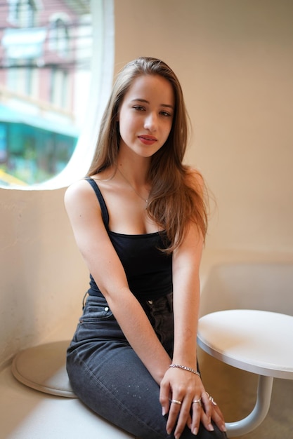 Photo young beautiful and attractive woman with long brown hair in a black dress at cafe against urban background.