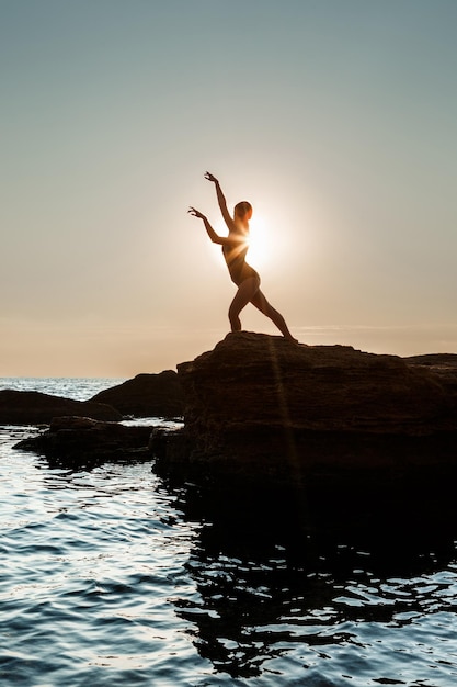 Young beautiful ballerina dancing, posing on rock at beach