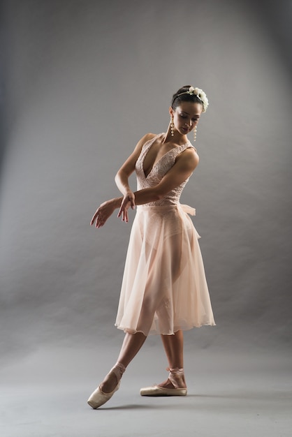 Young beautiful ballet dancer in beige swimsuit posing on pointes on light grey studio background