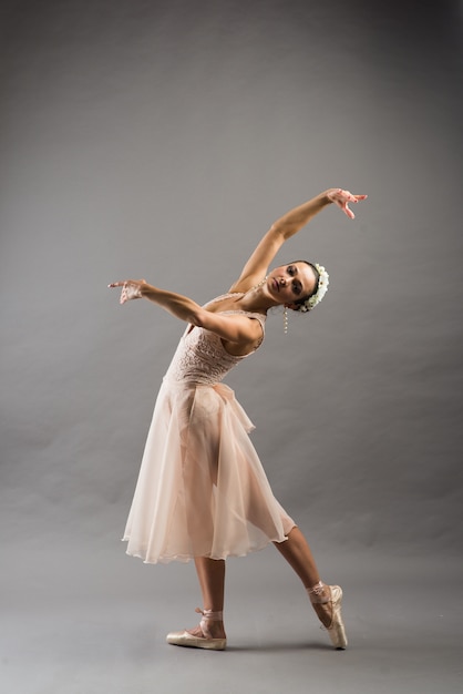 Young beautiful ballet dancer in beige swimsuit posing on pointes on light grey studio background