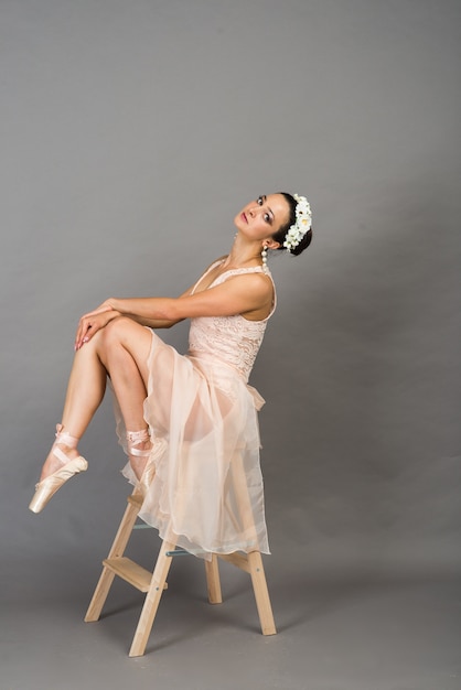 Young beautiful ballet dancer in beige swimsuit posing on pointes on light grey studio background