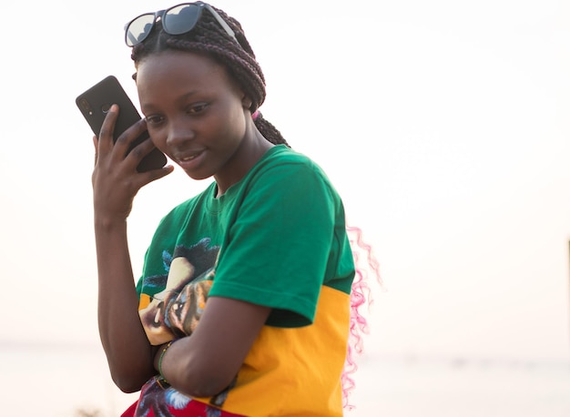 Young beautiful black girl using smart phone on sea beach at sunset