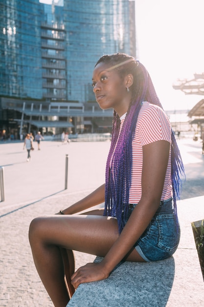 Young beautiful black woman sitting alone outdoor backlight pensive