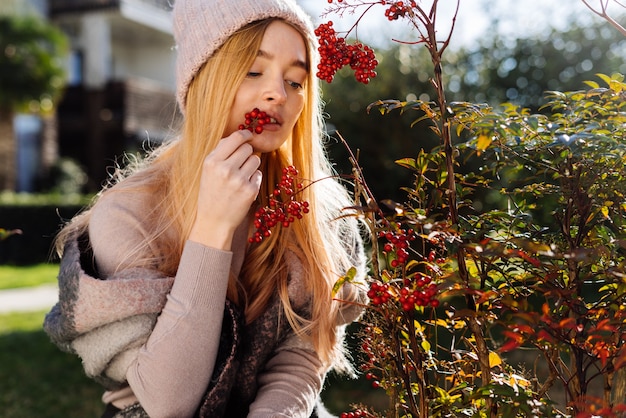 Young beautiful blond girl in a pink hat walking in the garden, trying the berries on the palate