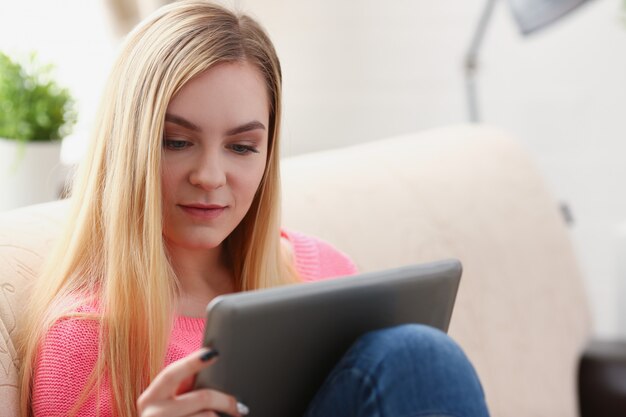 young beautiful blond woman sit on the sofa in livingroom hold tablet in arms