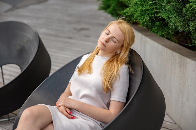 Young beautiful blond woman sitting outdoors on the wooden terrace in the city and resting Girl has break spending time outside and relaxing Time with yourself dreaming relaxation mental health