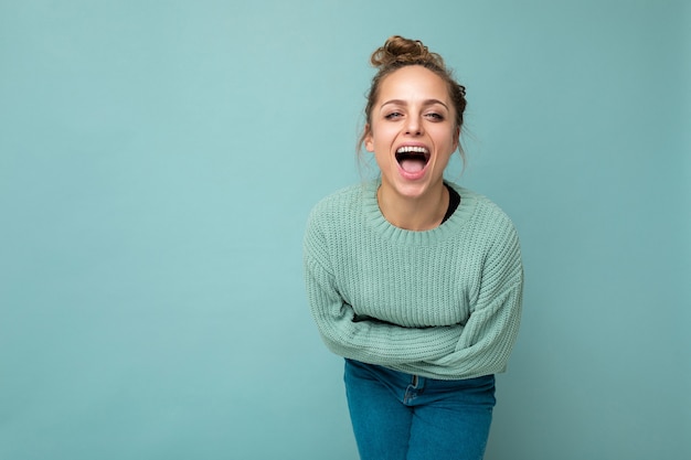 Young beautiful blond woman wearing blue pullover . Positive female shows facial sincere emotions. Funny model isolated on blue wall with empty space.