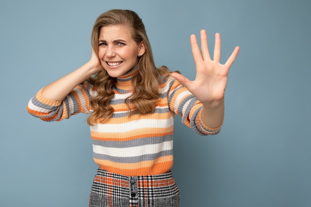 Young beautiful blonde curly woman with sincere emotions wearing stylish striped sweater isolated on