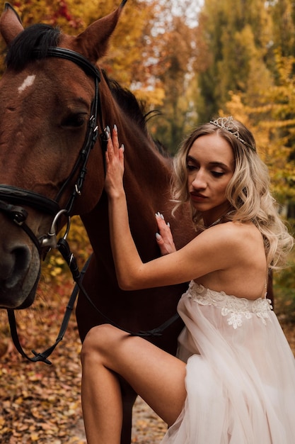 Young beautiful blonde girl posing in an autumn park with a horse