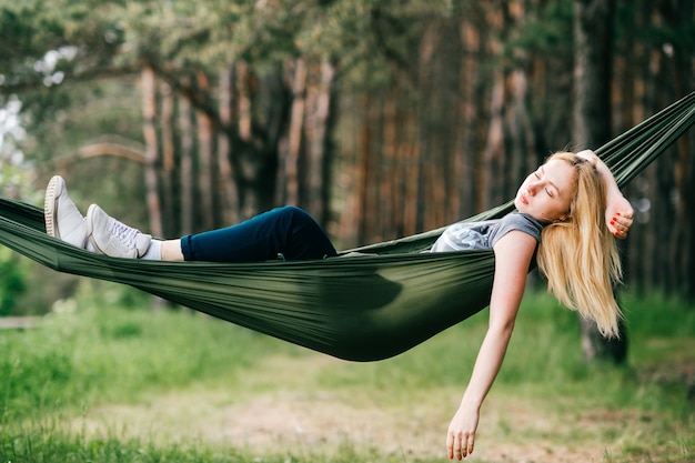 Young beautiful blonde girl relaxing in hammock at nature