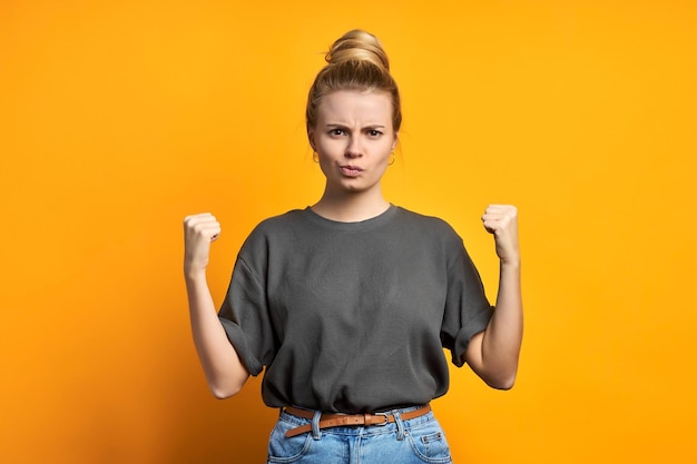 Young beautiful blonde sporty woman wearing casual sweatshirt over yellow background angry and mad raising fists frustrated and furious while shouting with anger Rage and aggressive concept