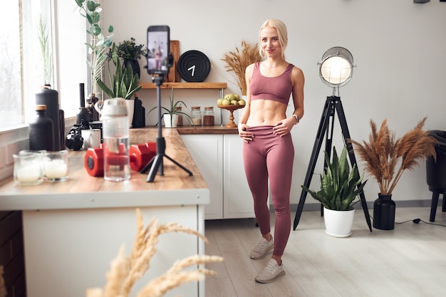 Photo young beautiful blonde takes care of her body while at home during quarantine. she trains people online through her mobile phone.