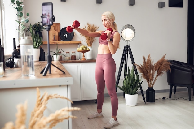 Photo young beautiful blonde takes care of her body while at home during quarantine. she trains people online through her mobile phone.