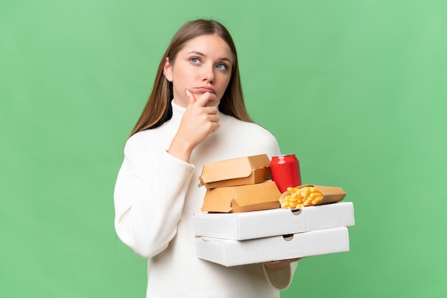 Young beautiful blonde woman holding takeaway food over isolated background having doubts