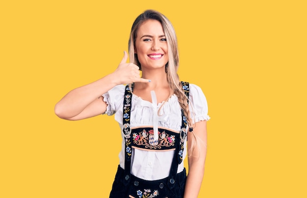 Photo young beautiful blonde woman wearing oktoberfest dress smiling doing phone gesture with hand and fingers like talking on the telephone communicating concepts