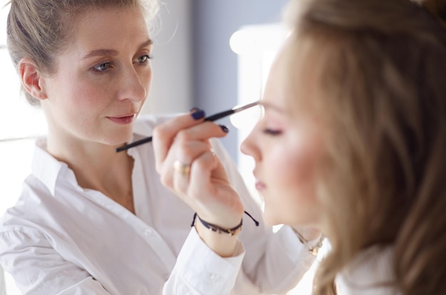 Young beautiful bride applying wedding makeup by professional makeup artist