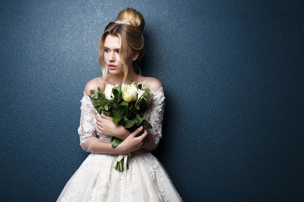 Young beautiful bride. Wedding hairstyle, blond hair, wedding dress, makeup and bride's bouquet. Indoor shot