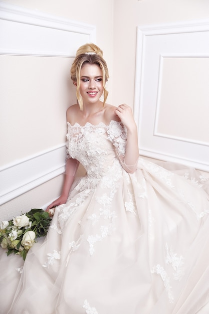 Young beautiful bride. Wedding hairstyle, blond hair, wedding dress, makeup and bride's bouquet. Indoor shot