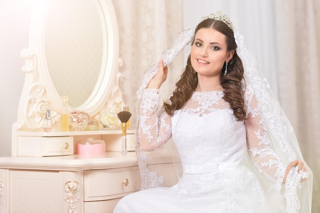 Young beautiful bride in white dress posing near the mirror