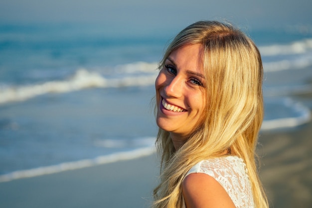 Young and beautiful bride with long blond hair beautifully smiling and walking on the sea in beautiful white long wedding dress. a happy bride married a wedding ceremony on the beach by the sea