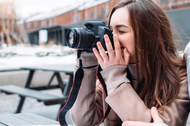 Young beautiful brunette girl photographer makes photos outdoor in cafe in winter cold weather