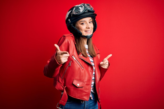 Young beautiful brunette motocyclist woman wearing motorcycle helmet and red jacket pointing fingers to camera with happy and funny face Good energy and vibes