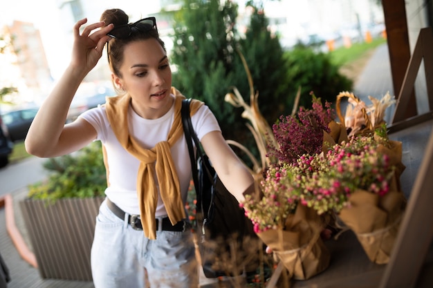 Young beautiful brunette woman enjoying flowers in pots on the porch of a flower shop