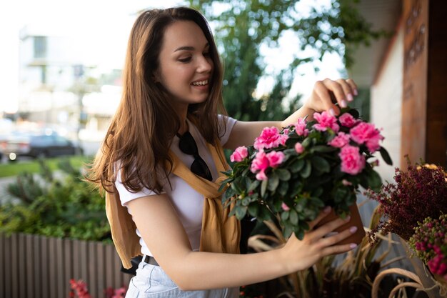 Young beautiful brunette woman enjoying flowers in pots on the porch of a flower shop