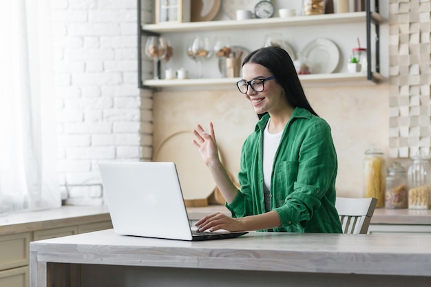 A young beautiful brunette woman in glasses and a green shirt is talking on a video call with