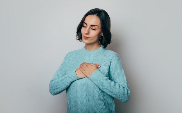 Young beautiful brunette woman in love holding herself chest and heart two hands with enjoying smiling face and thinking about relationship