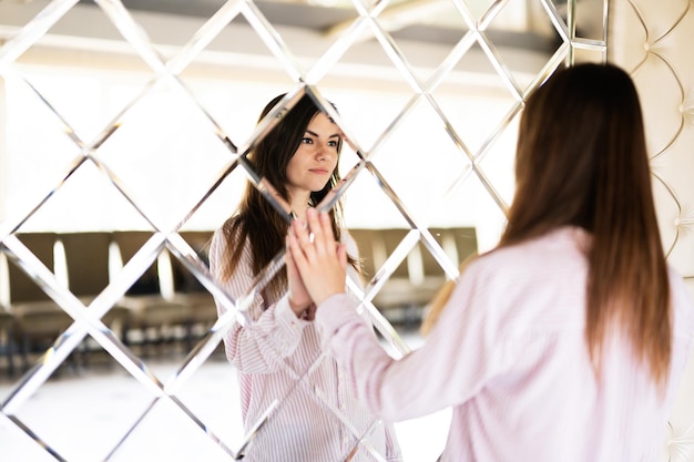 Young beautiful brunette woman in shirt touching mirror made of rhombuses