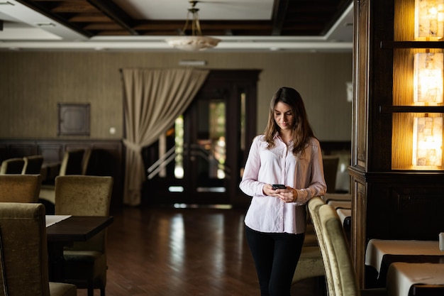 Young beautiful brunette woman stand in restaurant and look at phone