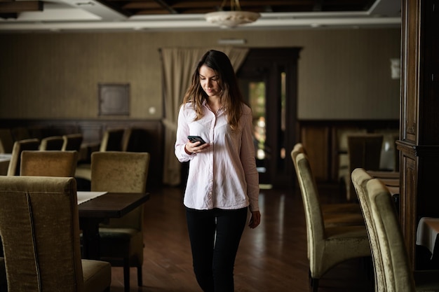 Young beautiful brunette woman walk in restaurant and look at phone