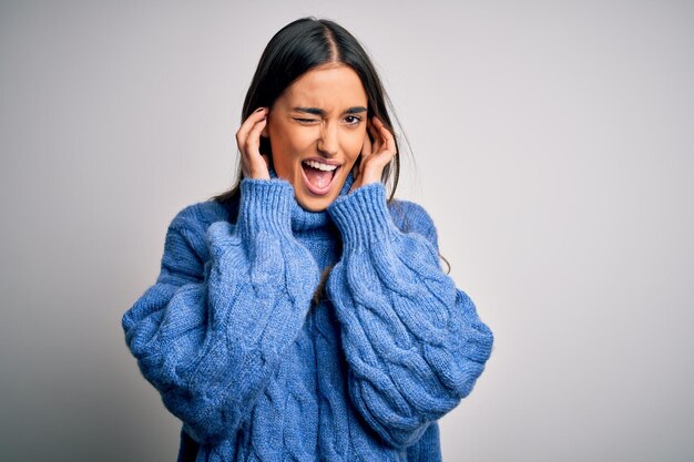 Young beautiful brunette woman wearing casual turtleneck sweater over white background covering ears with fingers with annoyed expression for the noise of loud music Deaf concept